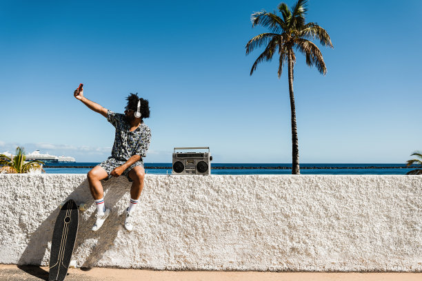 以海滩为背景自拍的非洲男子——专注于手持手机图片下载