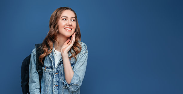 学生女孩与背包微笑，持有笔记本，抄写本，文件夹孤立在深灰色的背景图片下载