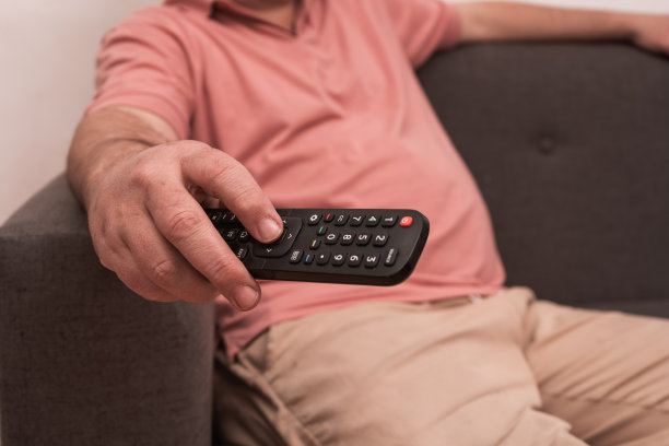 一个面目全的男人坐在沙发上，手里拿着遥控器在电视上换频道。图片下载