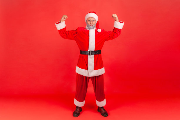 我很坚强!肖像自信自豪的老人与灰色胡子穿着圣诞老人服装展示力量在他的手，展示肱二头肌。图片下载
