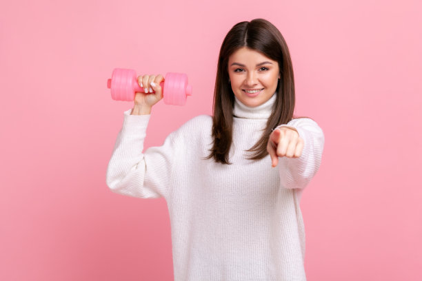 微笑的女性手持玫瑰哑铃，指着镜头，呼吁参加运动。图片下载