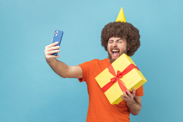 兴奋的积极男子手持礼盒和自拍或视频通话的肖像。图片下载