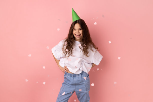 小女孩在派对锥站在飘落的五彩纸屑下，看着镜头，庆祝生日。图片下载