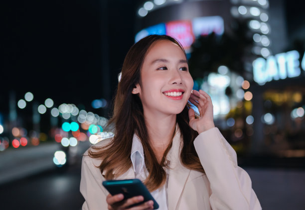 亚洲女商人晚上在现代城市里用无线耳机听音乐图片下载
