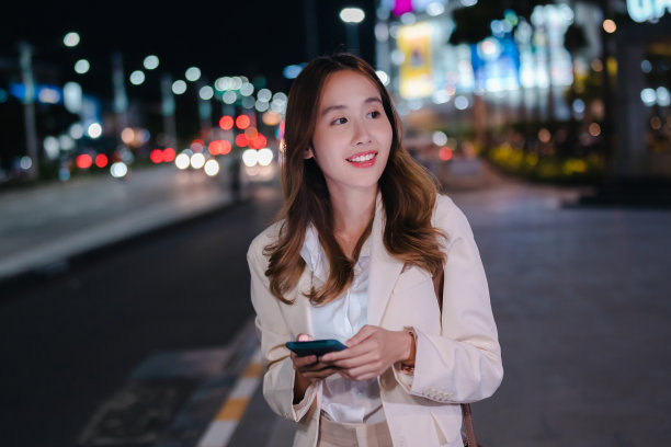 亚洲女商人晚上在现代城市里用无线耳机听音乐图片下载