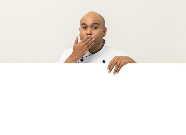 快乐的年轻英俊的亚洲人厨师在制服从一个空的白板后面看出去。做饭的印度人躲在厨房和餐厅的大空白广告牌后面为文本菜单做广告。图片下载