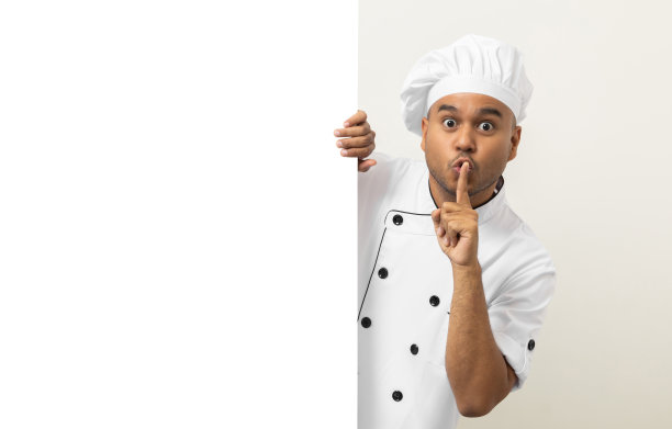 快乐的年轻英俊的亚洲人厨师在制服从一个空的白板后面看出去。做饭的印度人躲在厨房和餐厅的大空白广告牌后面为文本菜单做广告。图片下载