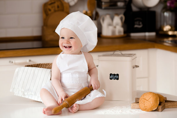 孩子们的厨师。漂亮的小男孩，围着白围裙，戴着厨师帽，手里拿着搅拌器。背景是厨房的内部。烹饪概念。图片下载
