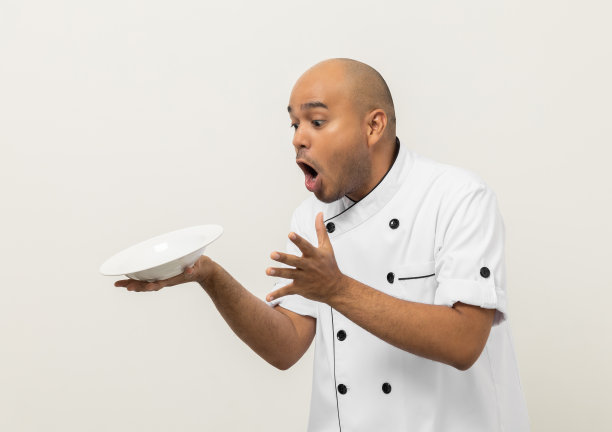 震惊的脸。年轻英俊的亚洲男子厨师在制服洒空盘子美味的菜菜单意外掉在孤立。印度人的职业厨师，厨房、餐厅和酒店的人。图片下载