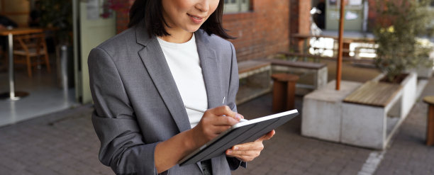 快乐的职业女性站在户外用电子平板电脑做笔记。图片下载