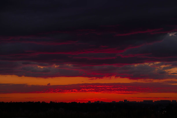 横幅。美丽的橙红色火红的日落在城市上空。天空中乌云密布。地平线上摩天大楼的轮廓。图片下载