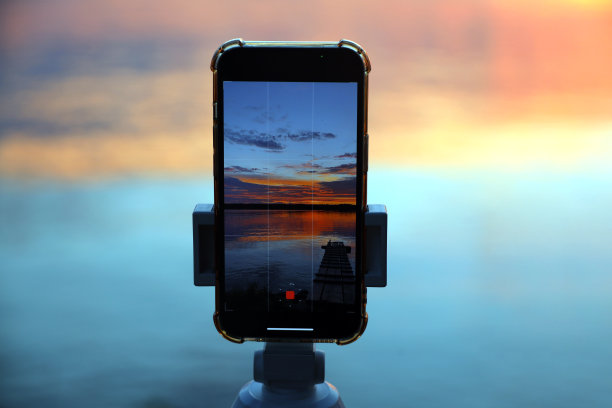 博主用智能手机在湖或河上拍摄日落，手机上的日落视频录制过程图片下载