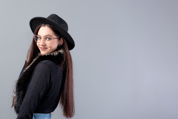 一个性感的女人的肖像，一头长发，头上戴着黑色的帽子，孤立在灰色的背景上图片下载