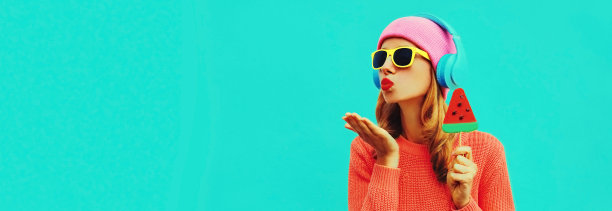 夏天清新多彩的肖像时尚的女人戴着耳机听音乐水果多汁的棒棒糖或冰淇淋形状的西瓜片在蓝色的背景图片下载