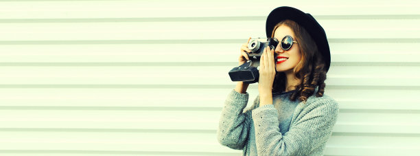 年轻女性摄影师肖像与胶卷相机穿针织毛衣开衫，黑色圆帽子在白色背景图片下载