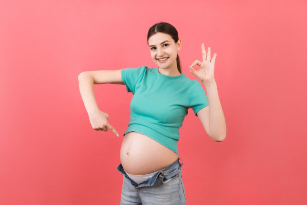 年轻美丽的少女怀孕期待婴儿在孤立的彩色背景微笑显示大肚子图片下载