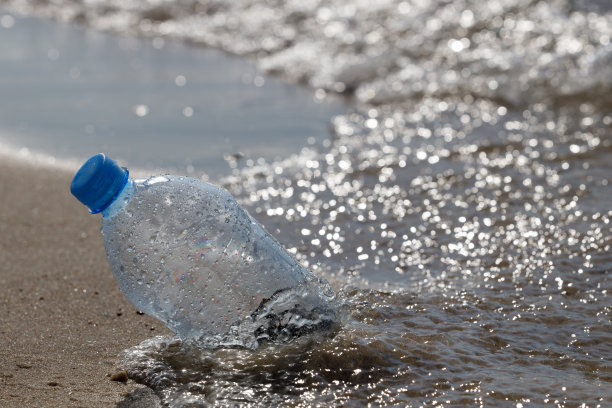 特写，选择性对焦，透明PET塑料瓶与蓝色的盖垃圾留在沙滩上图片下载