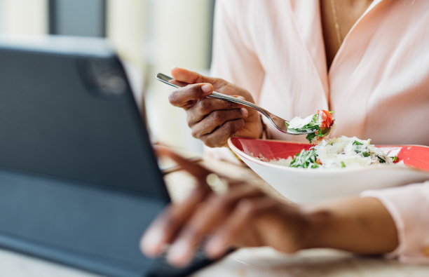 一位匿名女商人边吃午饭边玩平板电脑的特写图片下载