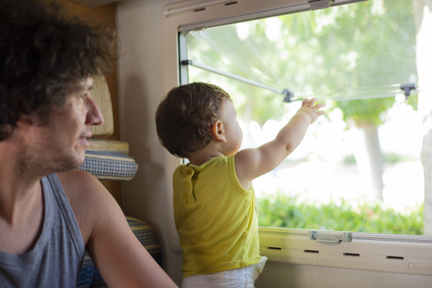 年轻的白人父亲和蹒跚学步的孩子看着窗外的房车或露营车图片下载
