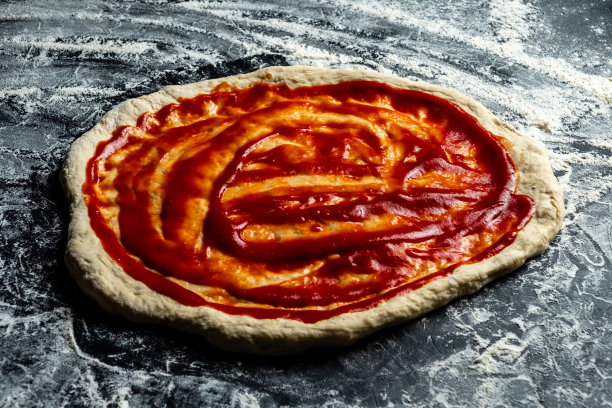 披萨面团涂上番茄披萨酱。黑暗的表。图片下载