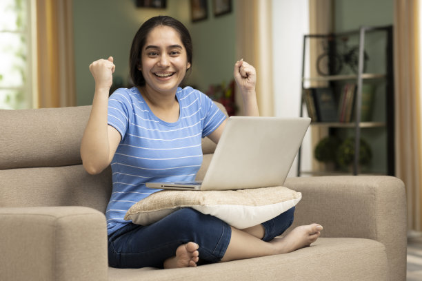 快乐微笑的女人坐在沙发上，使用笔记本电脑的股票照片图片下载