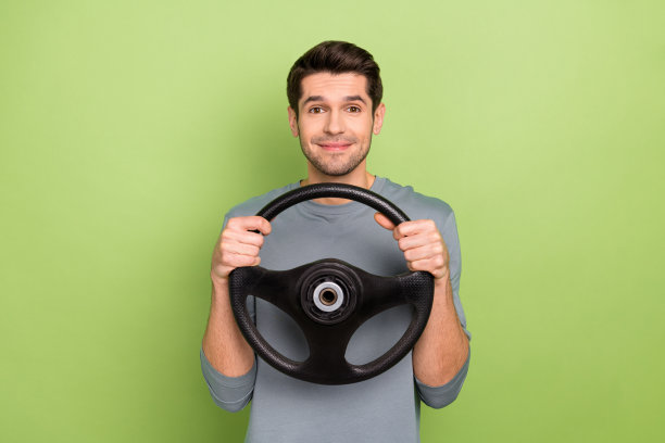 照片好年轻深色小伙子开车穿灰色套头衫孤立在绿色背景图片下载