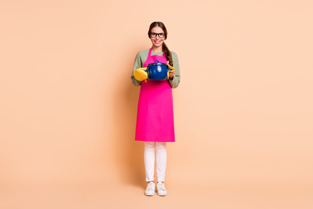 漂亮女孩穿着粉色围裙和眼镜，拿着平底锅，米色背景图片下载