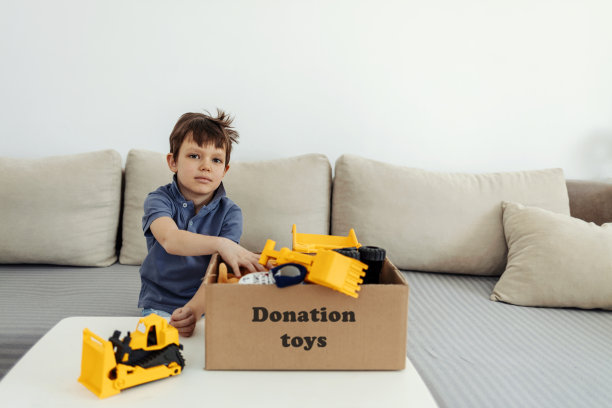 可爱的男孩拿着装满叠好的衣服和玩具的捐赠箱。图片下载
