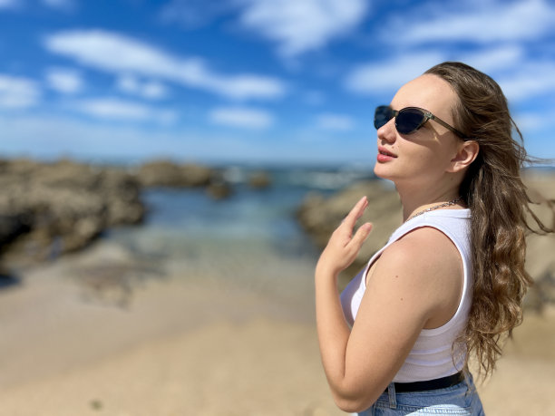 一个美丽的年轻女孩与金发和黑色墨镜站在大西洋的背景下，在葡萄牙，她穿着白色t恤和牛仔裤，有一个地方的文字图片下载