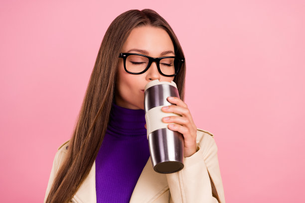 冷静的年轻女士喝美式咖啡的照片穿高领眼镜孤立在粉红色的背景图片下载