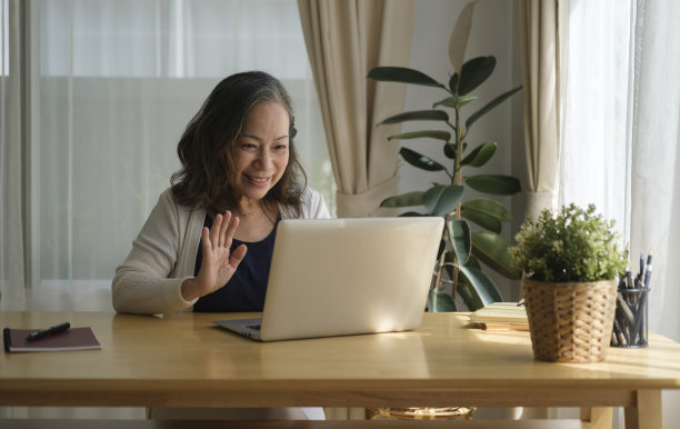 微笑成熟的女人坐在明亮的客厅里，用笔记本电脑进行视频通话。图片下载