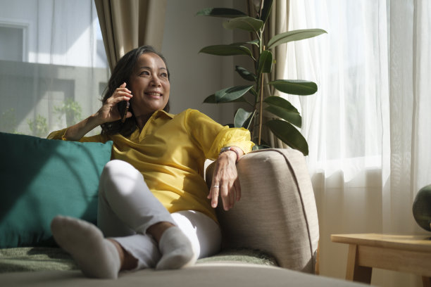 快乐的中年妇女休息在舒适的沙发上，讲手机。图片下载
