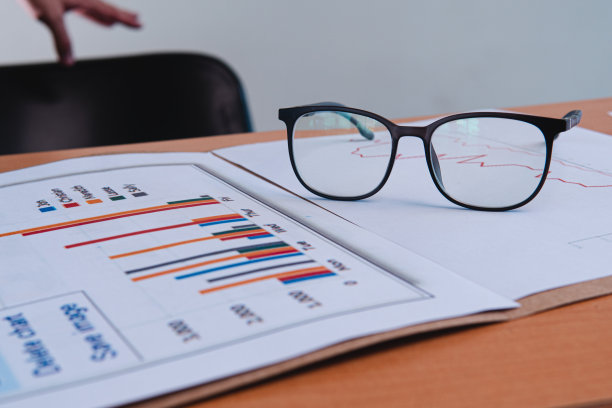 一个商人的工作台，上面放着纸、图表和眼镜。商业演示模板与文件，文件夹和一把椅子在背景。图片下载