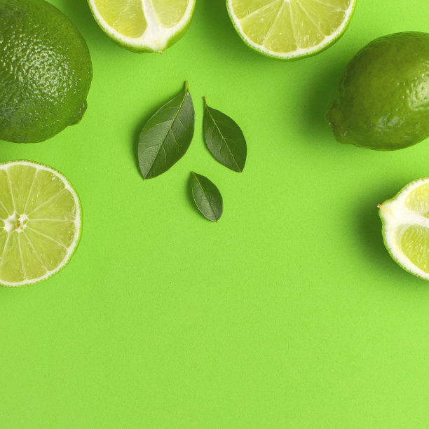 新鲜多汁的酸橙和绿色的叶子，底色明亮。俯视图平铺拷贝空间。创意食物背景，热带水果，维生素C，柑橘。与整个和切片的青柠组成图片下载