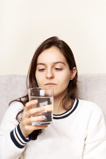 年轻女子坐在家里的沙发上，喝着一杯新鲜的水图片下载