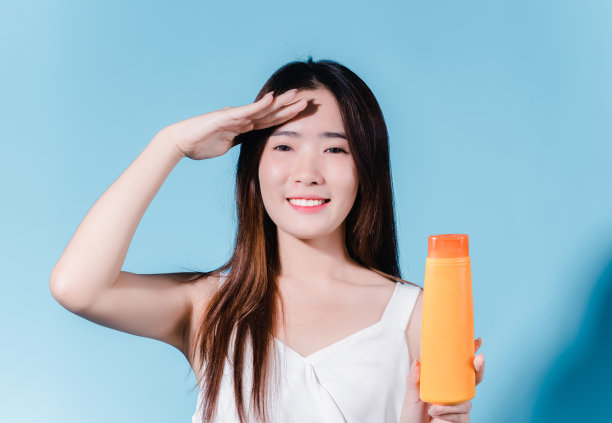 迷人的亚洲美女持有防晒霜和颜色规模与防晒紫外线或防晒霜的蓝色背景图片下载
