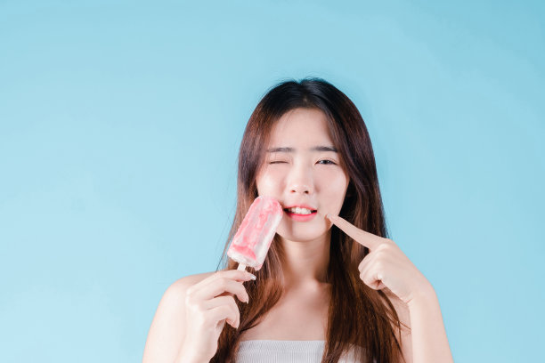 拿着冰棒的亚洲女性在蓝色背景上有一个敏感的牙齿图片下载