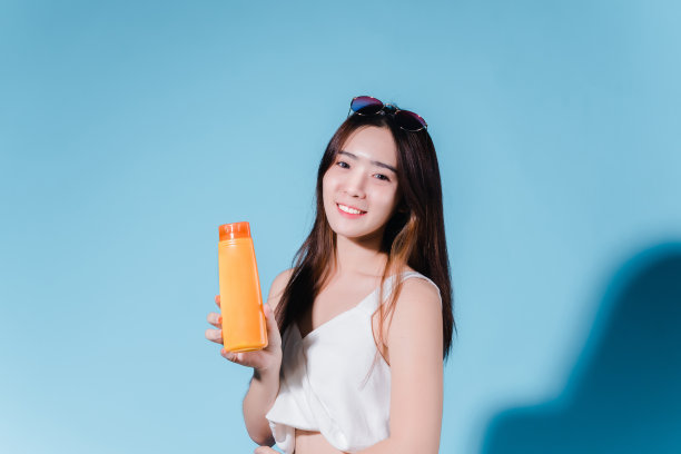 迷人的亚洲美女持有防晒霜和颜色规模与防晒紫外线或防晒霜的蓝色背景图片下载