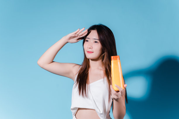 迷人的亚洲美女持有防晒霜和颜色规模与防晒紫外线或防晒霜的蓝色背景图片下载