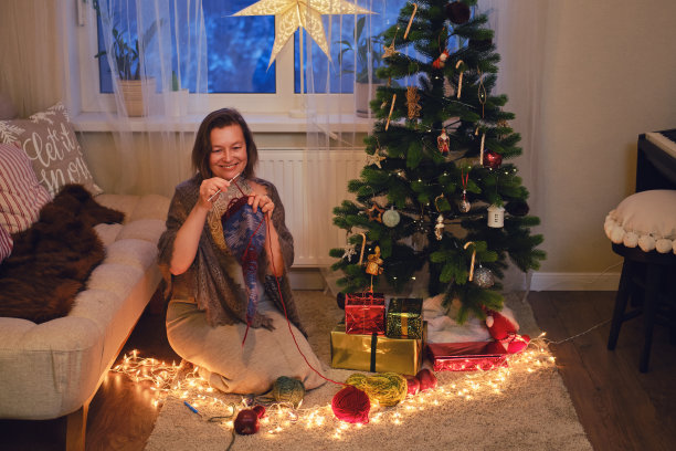 一名成年妇女在客厅的圣诞树旁织衣服。爱好并在除夕用毛线做针线活图片下载