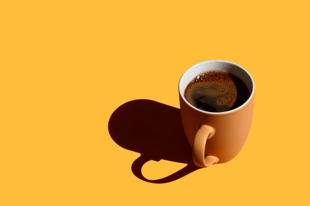 棕色杯子满咖啡与硬阴影在黄色的背景与拷贝空间图片下载