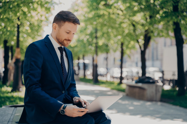 年轻的商人坐在城市公园的长椅上，用笔记本电脑工作图片下载