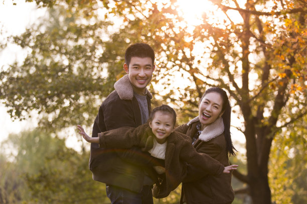 秋天夕阳下，父母抱着他们的女儿在五彩斑斓的丛林中，女孩张开双臂模仿航拍照片的翅膀图片下载
