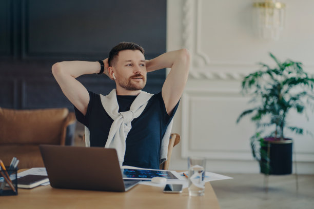 经验丰富的欧洲人坐在椅子上，看着远处，深思熟虑的表情，在家里的桌面姿势，办公室通过耳机听信息，使用免费的互联网连接，准备考试图片下载