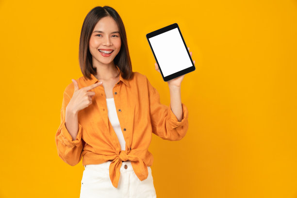 工作室拍摄的美丽的亚洲女人手持数字平板电脑模型的空白屏幕和微笑的橙色背景。图片下载