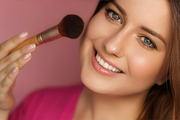 美丽的年轻女子应用化妆品粉产品与化妆竹刷，美容，化妆和护肤化妆品模型的脸肖像在粉红色的背景图片下载