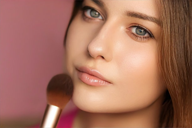 美丽的年轻女子应用化妆品粉产品与化妆竹刷，美容，化妆和护肤化妆品模型的脸肖像在粉红色的背景图片下载