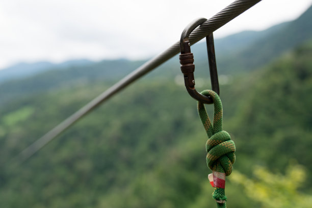 在锁扣上打结。登山者保险。绿山背景上的铁钩。图片下载