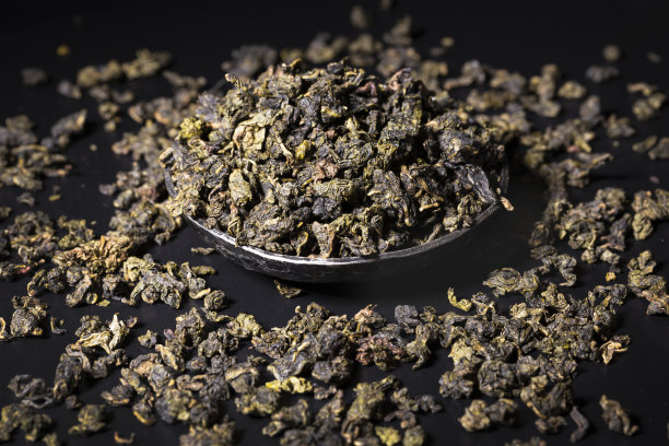 特写的干绿茶茶叶进入黑色碗在黑色的背景。图片下载