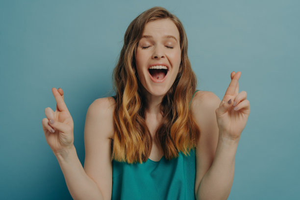 充满希望的女孩交叉手指，让愿望成真的姿态，眼睛闭着，她的嘴张开图片下载